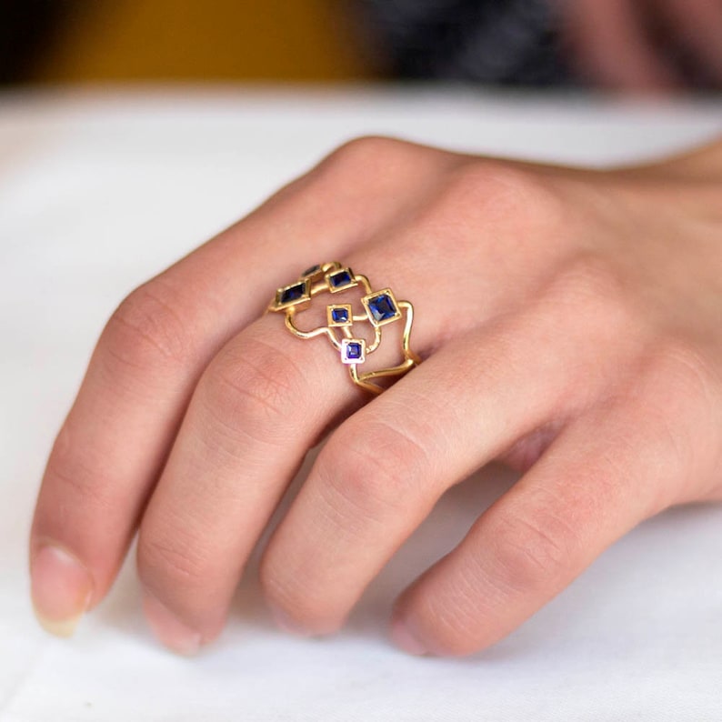 May include: A gold ring with a geometric design featuring multiple square-shaped blue gemstones.