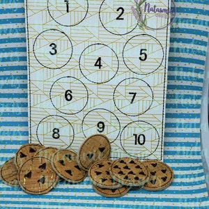 以下が含まれることがあります： 白いフェルトボードに、10個の番号付きの円がグリッド状に並んでいます。ボードは、茶色の蓋が付いた瓶の形をしています。ボードの下には、黒い模様が描かれた茶色のコルク円が10個あります。