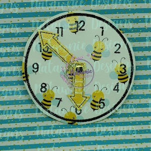 Könnte beinhalten: Ein weißes Zifferblatt mit schwarzen Zahlen und Bienenillustrationen. Die Uhrzeiger sind golden und zeigen auf die Zahl 4. Die Uhr befindet sich auf einem blau-weiß gestreiften Hintergrund.