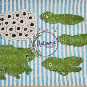 May include: A set of five green felt appliques depicting a frog, three tadpoles, and a cluster of frog eggs. The appliques are decorated with glitter and are perfect for crafting projects.
