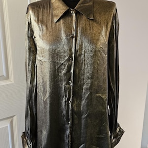 May include: A long-sleeved, button-down shirt in a shimmering gold color. The shirt has a classic collar and buttoned cuffs. The fabric has a metallic sheen, giving it a luxurious appearance. The shirt is displayed on a mannequin.