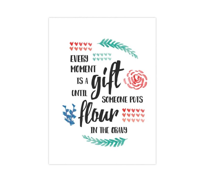以下が含まれることがあります： 「Every moment is a gift until someone puts flour in the gravy」というテキストが書かれた白い長方形のプリント。テキストは黒い筆記体で、赤いハート、緑の葉、ピンクのバラの水彩アクセントが施されています。