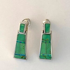 May include: A pair of silver dangle earrings with green turquoise stones. The stones are set in a geometric pattern.