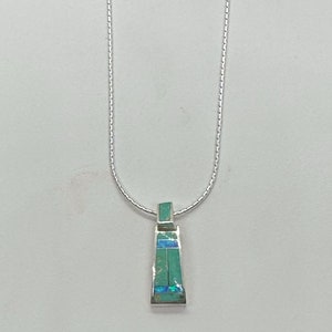 Puede incluir: Un collar de cadena de plata con un colgante de turquesa y ópalo. El colgante es de forma rectangular con un diseño geométrico.
