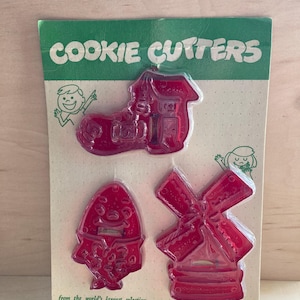 May include: A set of three red plastic cookie cutters on a green and white display card. The shapes include a shoe, a character resembling Humpty Dumpty, and a windmill. The card features the text COOKIE CUTTERS and from the world's largest selection.