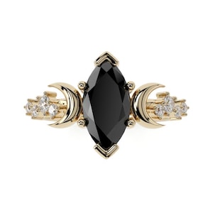 Könnte beinhalten: Ein goldener Ring mit einem schwarzen, markisenförmigen Edelstein und zwei Halbmond-Akzenten auf jeder Seite. Der Ring ist mit kleinen, klaren Edelsteinen besetzt.