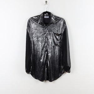 May include: A silver and black long-sleeved shirt with a floral pattern and a pocket on the left side. The shirt has a button-up collar and a label that says "L.A.N.Y."