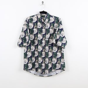 May include: A short-sleeved button-down shirt with a navy blue, green, and white geometric pattern. The pattern features a repeating design of circles with a stylized image inside each circle.