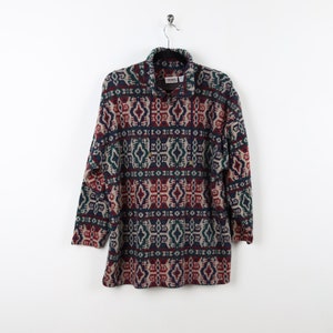May include: A long-sleeved patterned fleece jacket in shades of red, teal, navy, and beige hangs from a metal hanger. The jacket features a geometric design and a collared neckline with a partial zipper.