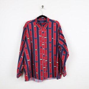 Puede incluir: Una camisa de manga larga con botones de rayas rojas y azules con un patr&oacute;n geom&eacute;trico. La camisa tiene un bolsillo en el pecho izquierdo y una etiqueta de marca en el cuello.