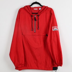 May include: A red windbreaker jacket with a hood and a half-zip closure. The jacket features a front pocket and the "Marlboro Unlimited" logo patch on the sleeve. The jacket is hanging on a black hanger.