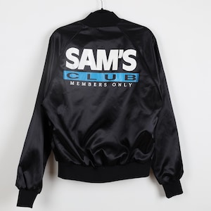 May include: Black satin bomber jacket with the text "SAM'S CLUB" in white block letters and a blue stripe with "CLUB" printed on the back. The jacket has a black collar, cuffs, and waistband. "MEMBERS ONLY" is printed below the blue stripe.