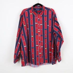 Puede incluir: Una camisa de manga larga con botones a rayas rojas y azules con un patr&oacute;n geom&eacute;trico. La camisa tiene un bolsillo en el lado izquierdo y una etiqueta de marca en el cuello.