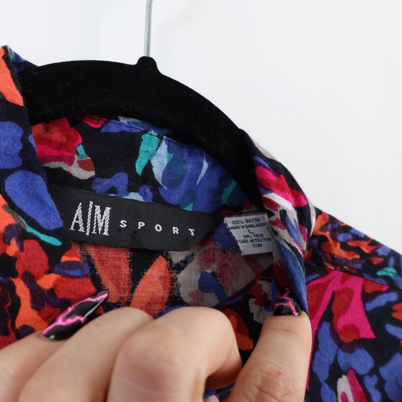 May include: A black, blue, red, and green floral print shirt with the text "AIM SPORT" on the collar. The shirt is made of 100% rayon and made in Bangladesh.
