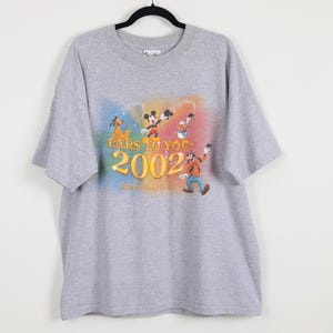 Pode incluir: Camiseta cinza com os personagens da Disney Mickey Mouse, Pato Donald, Pateta e Pluto. A camisa tem o texto "EARS TO YOU! 2002" e o logotipo da Walt Disney World. O gr&aacute;fico &eacute; colorido e em um fundo suave.