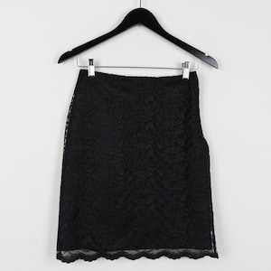 May include: A black lace skirt hangs from a black hanger against a white background. The skirt is knee-length with a scalloped hemline. The lace pattern is intricate and covers the entire skirt.