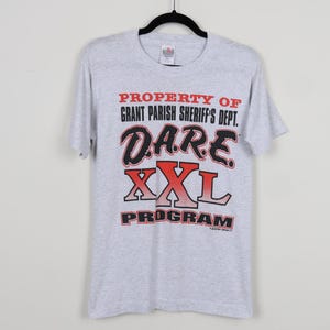 May include: Gray t-shirt with the text "PROPERTY OF GRANT PARISH SHERIFF'S DEPT. D.A.R.E. XXL PROGRAM" in black and red lettering.