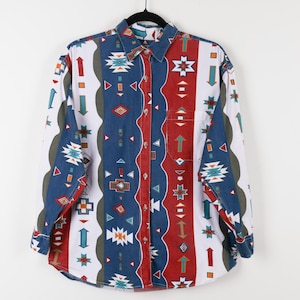 May include: A long-sleeved button-down shirt with a colorful geometric pattern. The shirt features a mix of red, blue, white, and green vertical stripes with arrows, diamonds, and starburst designs. It has a collared neckline and a single chest pocket.