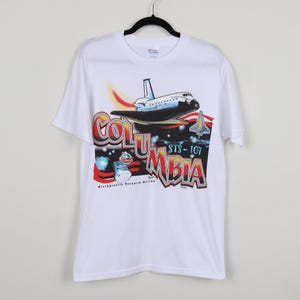 May include: White t-shirt with a colorful graphic of the Space Shuttle Columbia, with the text "Columbia" and "STS-107" printed on the front. The graphic also includes the text "Microgravity Research Mission".
