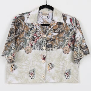 May include: A cropped, short-sleeved button-up shirt with a white background and a colorful print of lions and other jungle animals. The shirt has a button-up collar and a relaxed fit.