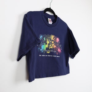 May include: A navy blue cropped t-shirt with a rainbow graphic of fireworks and the text "Girl Scouts Celebrating 100 Years Girl Scouts of Santa Clara County".