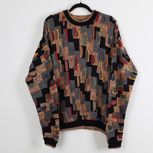 May include: A vintage, oversized sweater with a unique geometric pattern. The sweater features a mix of colors including black, brown, gray, red, yellow, and green. It has a crew neck and long sleeves, perfect for cooler weather.