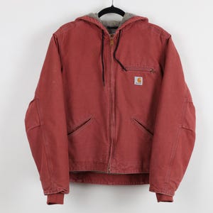 May include: A red hooded jacket with a full-length zipper and multiple pockets. The jacket has a soft, gray lining in the hood and a small logo patch on the chest. The jacket is hanging on a black hanger.