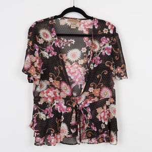 May include: A black sheer top with a floral print in shades of pink, red, and white. The top has a V-neckline and a tie at the waist. The label "Notations" is visible on the front.