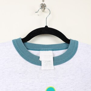 Puede incluir: Camiseta gris con cuello de canal&eacute; turquesa y una etiqueta de marca "Sandlot" blanca.