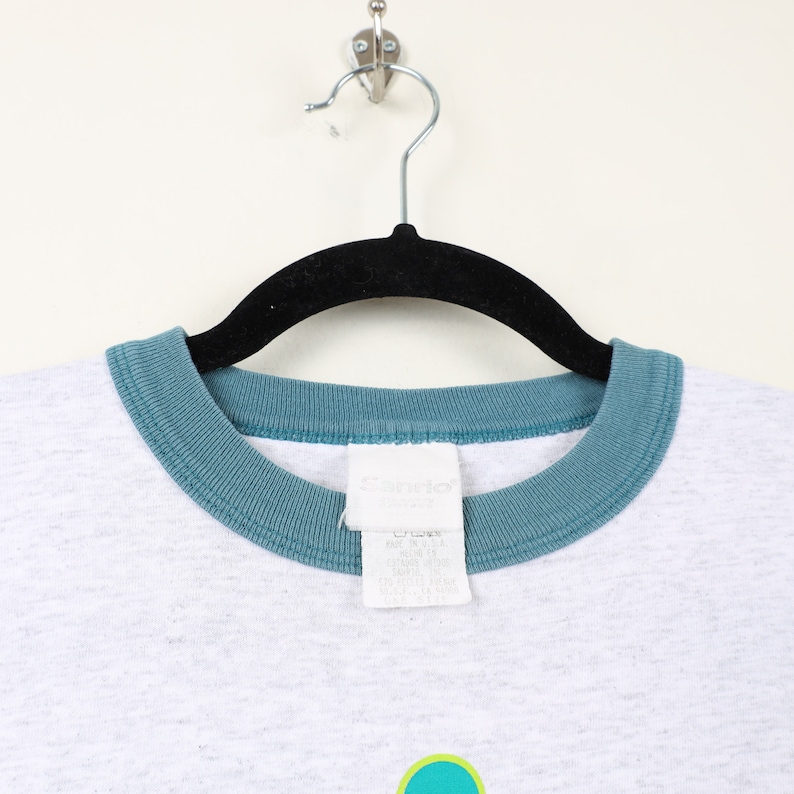 Puede incluir: Camiseta gris con cuello de canal&eacute; turquesa y una etiqueta de marca "Sandlot" blanca.