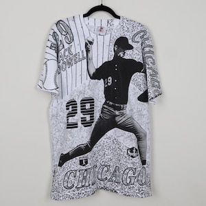 May include: Black and white vintage t-shirt featuring a baseball player in a pitching pose. The shirt has a distressed look with a baseball diamond pattern and the text "Chicago" and "Jack Powell" printed on it.