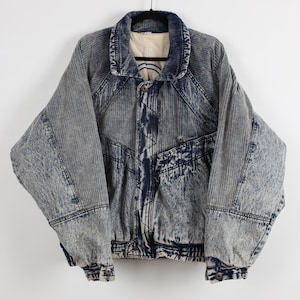 May include: Acid wash denim jacket with a button-up front, two front pockets, and a corduroy collar. The jacket has a light blue and dark blue color scheme, with a ribbed texture on the sleeves and body. The jacket is hanging on a black hanger.