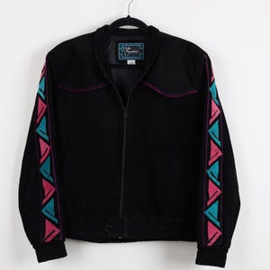 May include: Black corduroy jacket with a zip-up front, featuring geometric patterns in teal and pink on the sleeves. The jacket has a small label that reads "Echo Mountain". The collar and upper chest have a purple trim.