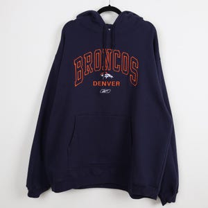 May include: Navy blue hoodie with the word "BRONCOS" in orange block letters across the chest. Below the word "BRONCOS" is the word "DENVER" and a logo. The hoodie has a front pocket and a hood.