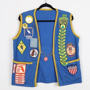 May include: Blue vest with yellow trim and numerous embroidered patches, including the text "NCHA" and "Past Chapter Officer", as well as various dates and logos.