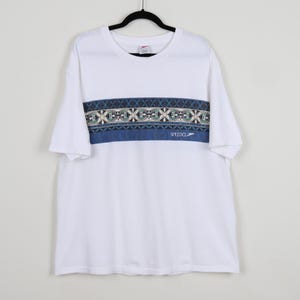 May include: White short-sleeved t-shirt with a blue and white patterned band across the chest. The band features a geometric design and the word "SPEEDO" in white.