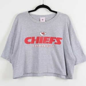 May include: A gray, short-sleeved t-shirt with the word "CHIEFS" in red block letters and the words "KANSAS CITY" underneath. The shirt also features the NFL logo.