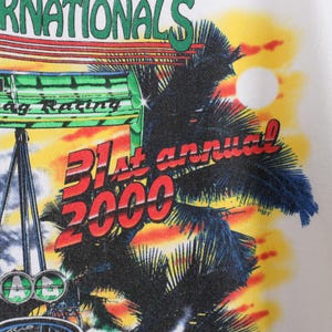 May include: White t-shirt featuring a colorful graphic design. The design includes the text "INTERNATIONALS" in green, "Drag Racing" in green, and "31st annual 2000" in red. A palm tree and a sunset are also depicted.