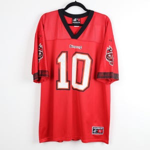 May include: A red mesh football jersey with a black V-neck collar. The front features the white number 10 with black trim and the word Buccaneers. Each sleeve displays a pirate ship logo. A Logo Athletic tag is visible at the bottom hem.