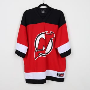 May include: Red, black, and white hockey jersey with the New Jersey Devils logo. The jersey has a v-neck and is size XL.