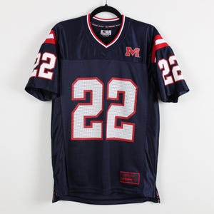 May include: Navy blue football jersey with the number 22 in white and red on the front and sleeves. The jersey has a V-neck collar with red and white trim and the letter "M" on the chest.