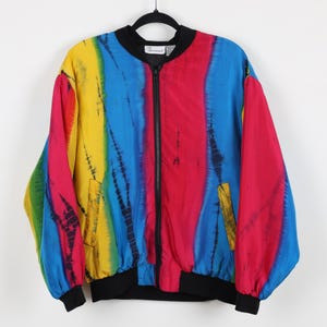 May include: A vibrant, tie-dye bomber jacket in a rainbow of colors: yellow, blue, red, and green. The jacket has a black zipper, cuffs, and collar. The jacket is hanging on a black hanger.