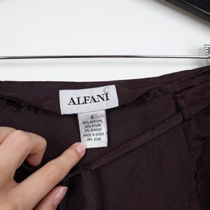K&ouml;nnte beinhalten: Eine dunkelbraune Hose mit einem Stofflabel, auf dem "ALFANI" steht, und einem Gr&ouml;&szlig;enetikett mit der Aufschrift "4 58% Acetat 21% Nylon 3% Elasthan Hergestellt in Korea WPL 8046".