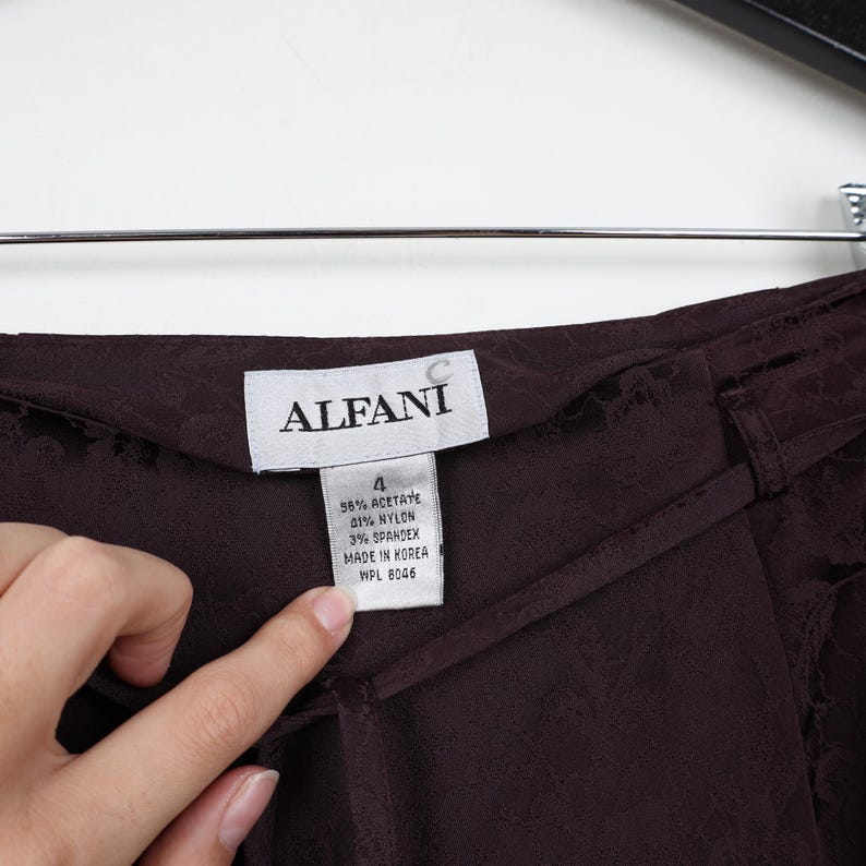 K&ouml;nnte beinhalten: Eine dunkelbraune Hose mit einem Stofflabel, auf dem "ALFANI" steht, und einem Gr&ouml;&szlig;enetikett mit der Aufschrift "4 58% Acetat 21% Nylon 3% Elasthan Hergestellt in Korea WPL 8046".