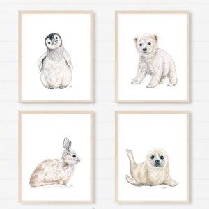 May include: Four framed art prints featuring watercolor illustrations of a penguin, polar bear cub, rabbit, and seal pup. The prints are displayed above a white crib. The text "Fine Art Prints By JAMES RIVER STUDIOS" is visible.
