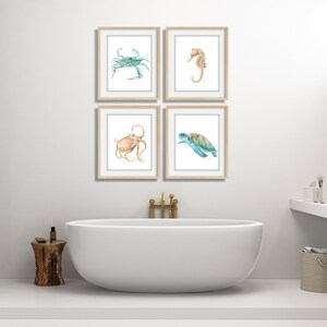 Puede incluir: Cuatro acuarelas enmarcadas de criaturas marinas. Las pinturas representan un cangrejo azul, un caballito de mar, un pulpo y una tortuga marina. Las pinturas est&aacute;n colgadas en una pared blanca sobre una ba&ntilde;era blanca.