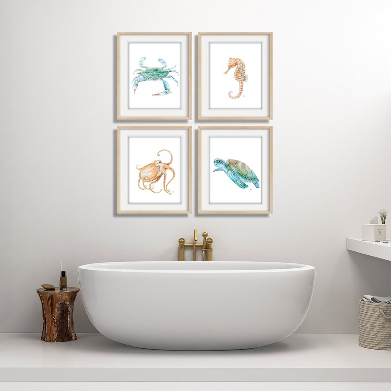 Puede incluir: Cuatro acuarelas enmarcadas de criaturas marinas. Las pinturas representan un cangrejo azul, un caballito de mar, un pulpo y una tortuga marina. Las pinturas est&aacute;n colgadas en una pared blanca sobre una ba&ntilde;era blanca.