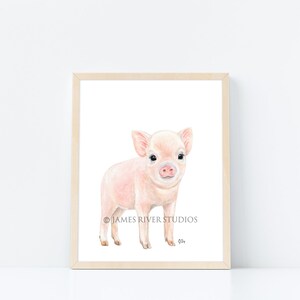 Puede incluir: Una pintura de acuarela de un lech&oacute;n rosado de pie sobre un fondo blanco. El lech&oacute;n tiene un hocico rosado, ojos negros y un cuerpo rosado. La pintura est&aacute; enmarcada en un marco de madera claro.