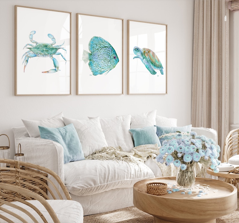 May include: Three framed watercolor paintings of sea life. The first painting features a blue crab, the second painting features a blue and green fish, and the third painting features a green sea turtle.