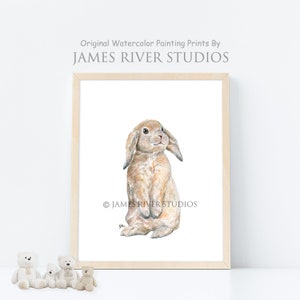 May include: A watercolor painting of a brown lop-eared rabbit standing on its hind legs. The rabbit has a white nose and white markings on its face. The painting is framed in a light wood frame. &copy; JAMES RIVER STUDIOS